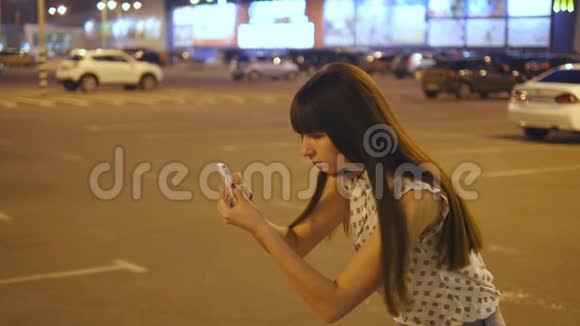 年轻女子在购物中心停车场玩口袋妖怪使用智能手机晚上的女孩扮演流行的角色视频的预览图