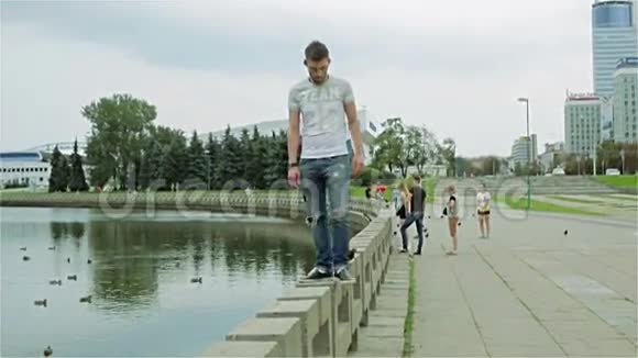 一个留着胡子的年轻人从河的混凝土栅栏上跳下来沿着人行道走视频的预览图