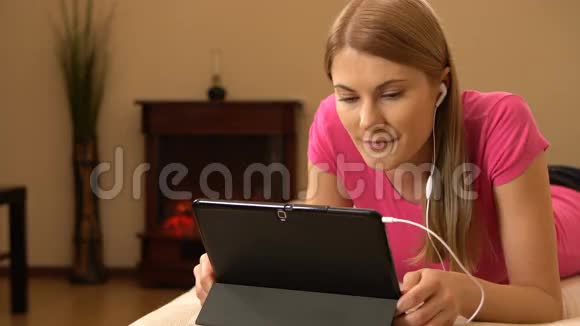 美丽迷人的年轻女人躺在沙发上在平板电脑上看电影笑着00337视频的预览图