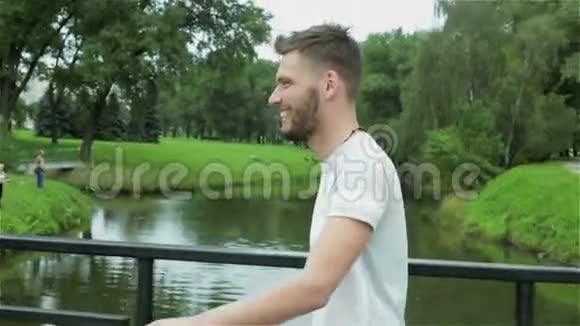 一个留着胡子的年轻帅哥正走在河对岸的一座小桥上视频的预览图