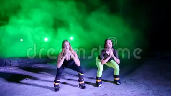 两名运动女性晚上在轻烟雾中做各种健身运动腿上有重量视频的预览图