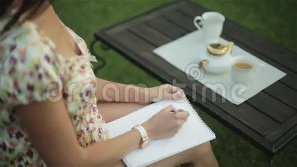 一个穿睡衣的漂亮女人在外面吃早餐在她腿上的纸上写了一封信视频的预览图