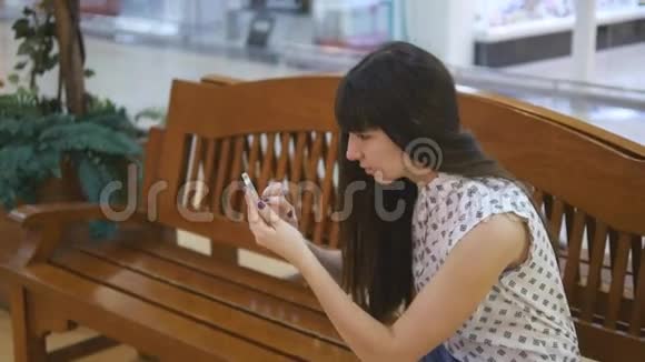 玩口袋妖怪的年轻女子在购物中心用智能手机进入室内坐在板凳上玩大众游戏的女孩视频的预览图