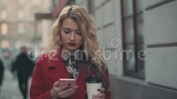 商务女性穿着红色外套带着咖啡在城市里散步并通过智能手机phablet进行交流稳住摄像机视频的预览图