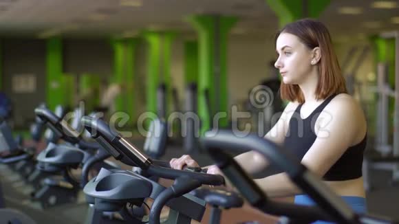 在绿色体育馆里这位妇女在健身车上锻炼肌肉的侧面特写照片视频的预览图