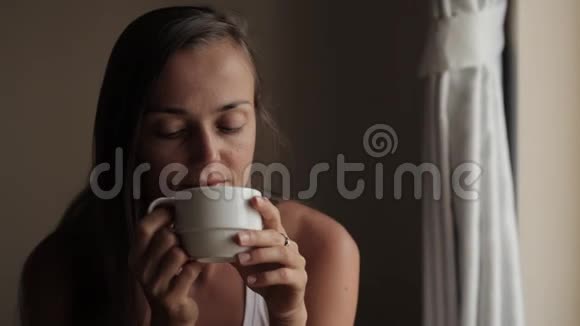 年轻迷人的女人望着窗户喝茶视频的预览图