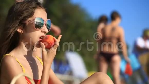 长发女孩在海浪背景下拥挤的海滩上吃水果和浆果视频的预览图