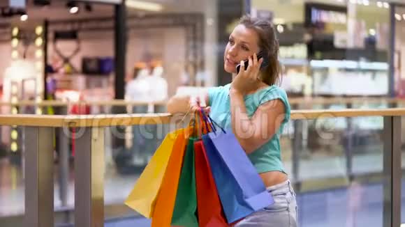 带着纸袋在购物中心的智能手机上说话的女人视频的预览图