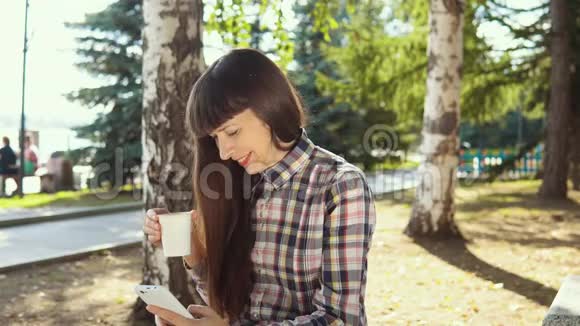 一位身穿连帽衫的年轻女子在秋季公园使用智能手机视频的预览图