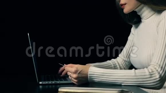 美丽的黑发女人用她的信用卡和笔记本电脑支付黑色背景网上购物视频的预览图