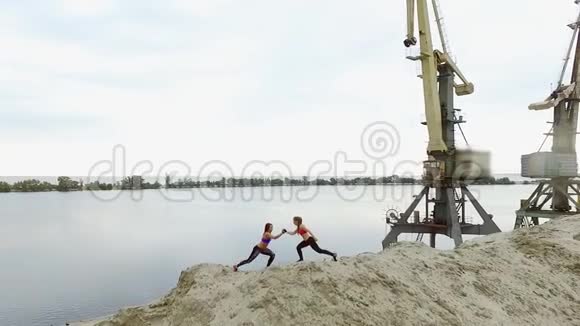 两个年轻的女运动员在采石场的沙地上做户外运动在背景上可以看到视频的预览图