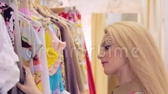 金发女人在精品店的特写镜头中选择衣架上的衣服视频的预览图