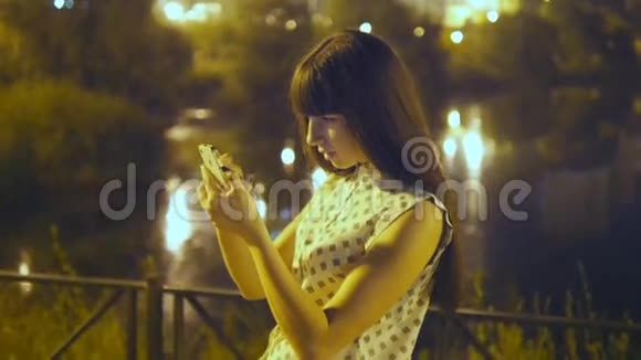 年轻女子晚上玩口袋妖怪去户外使用智能手机女孩玩流行的智能手机游戏捕捉视频的预览图