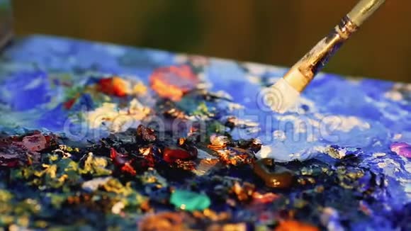 画家用画笔将彩色油画画在调色板上手中握着特写视频的预览图