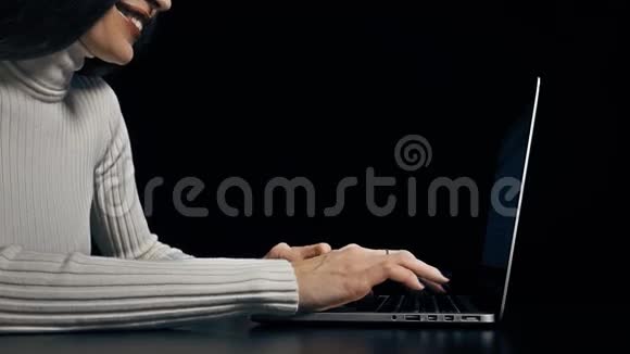 年轻的黑发女人在黑色背景下的笔记本电脑上打字4K视频视频的预览图