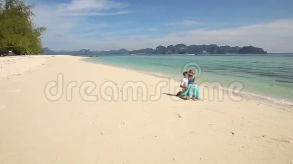 男人和金发女孩坐在海滩上的石头上视频的预览图