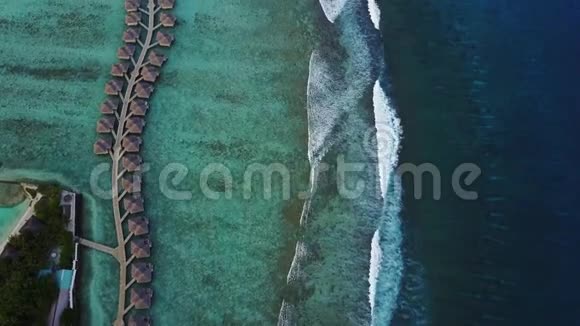 在马尔代夫有平房和绿松石印度洋海浪的热带岛屿度假酒店的空中景色从上面可以看到视频的预览图
