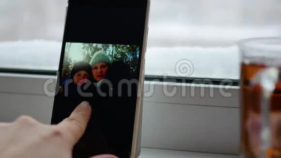 女孩在窗户附近喝茶用智能手机看照片视频的预览图