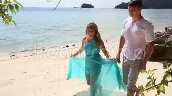 穿蓝色连衣裙的金发女孩和男朋友沿着海滩散步视频的预览图