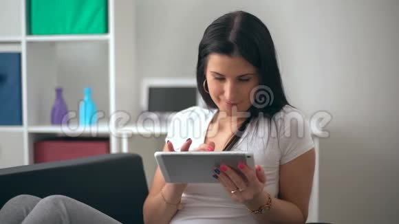 年轻女子在客厅的家里用平板电脑在沙发上放松视频的预览图