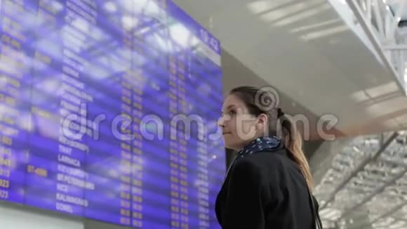 穿黑色夹克的女孩正在看机场的日程安排视频的预览图