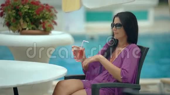 在度假泳池附近喝热带鸡尾酒的年轻时尚美女视频的预览图