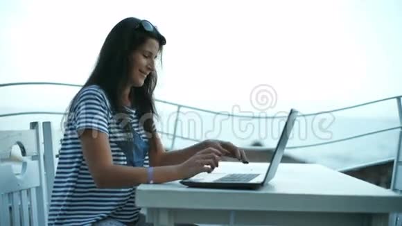 旅游女孩在海滩上的小吃店露台上使用笔记本电脑度假视频的预览图