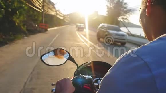 英俊的男子驾驶摩托车在热带岛屿在美丽的日落时慢动作而旅行泰国看法视频的预览图