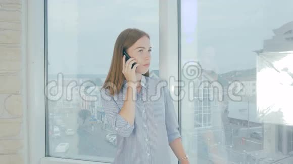 女士在办公室用手机站在办公室的窗户前视频的预览图