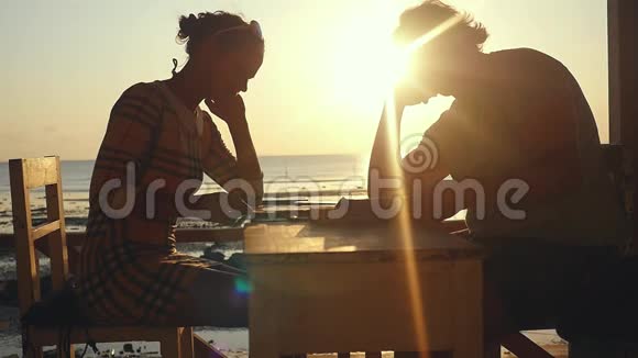 日落时分在海滩咖啡馆里有菜单和智能手机的年轻夫妇慢动作1920x1080视频的预览图