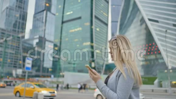 在市中心摩天大楼和高楼大厦的背景下一个金发女孩正在打电话视频的预览图