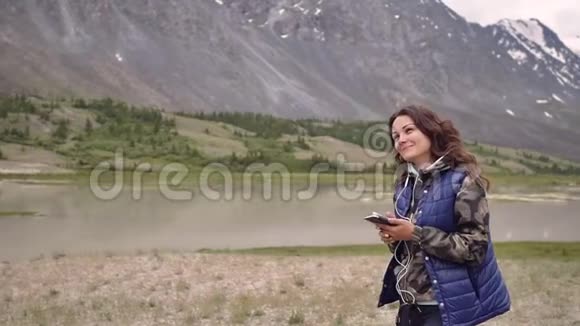 女游客戴着耳机在群山和风景的背景下跳舞旅游观光视频的预览图