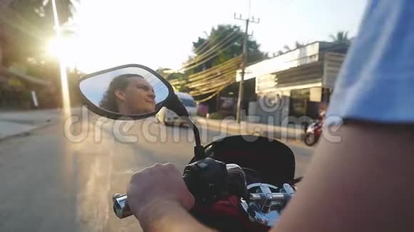 在美丽的日落中年轻的胡须男在热带岛屿上驾驶摩托车在旅行时慢动作泰国视频的预览图