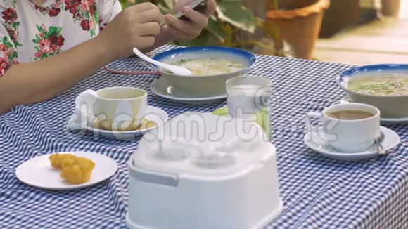 女人一边吃早饭一边玩智能手机视频的预览图
