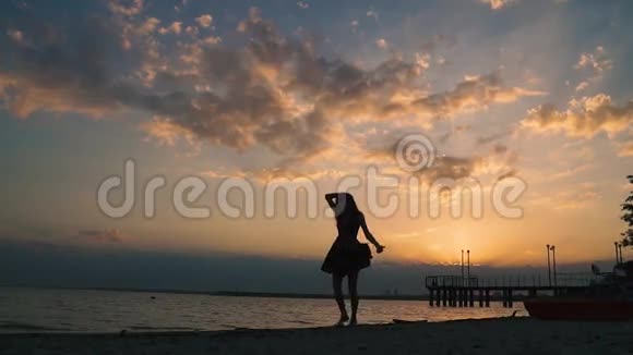 日落时分一个迷人的女孩赤脚在沙滩上散步的肖像一个漂亮女孩的剪影视频的预览图