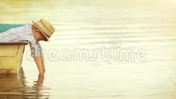 阳光明媚的画面一个男孩坐在船上靠在船板上把手伸进水里视频的预览图