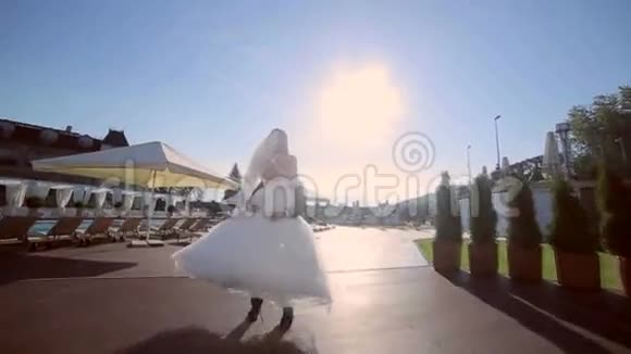 新婚夫妇快乐新郎双手抱着新娘绕着背景和明亮的太阳的水池旋转视频的预览图