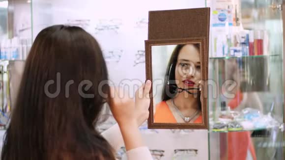 年轻女子在眼镜店用镜子检查她的新眼镜戴眼镜的年轻女子视频的预览图