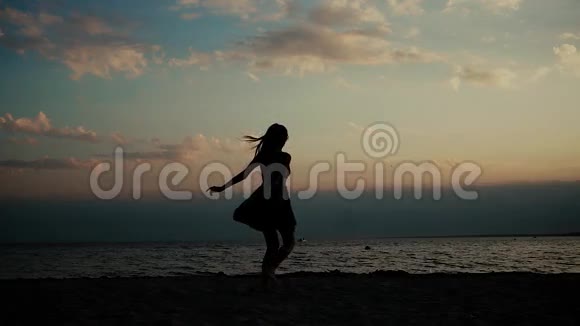 美丽快乐的女孩在海滩上旋转快乐地挥动着她的手臂日落时的剪影日落时分的年轻女子视频的预览图