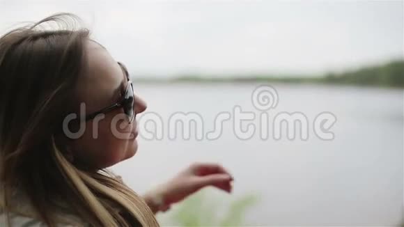 年轻漂亮的女人正在摘下太阳镜欣赏春天的湖景视频的预览图