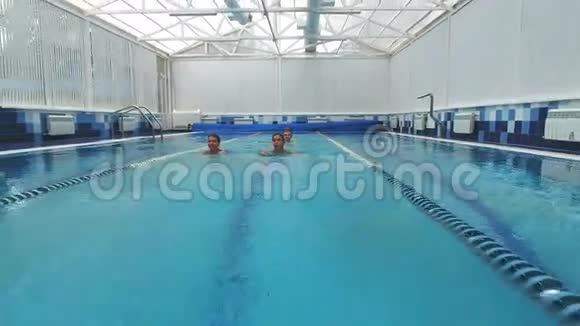 两个年轻的女人在游泳池里游泳一个年轻人在他们身后游泳视频的预览图