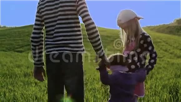 三个孩子在蓝天背景下走在绿色的草地上视频的预览图