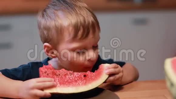 坐在厨房桌子旁的可爱小男孩的特写镜头孩子拿着一块吃着西瓜视频的预览图