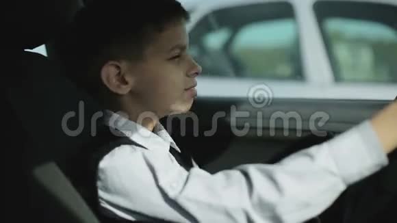 严肃的小学生正坐在汽车方向盘后面用手机说话视频的预览图