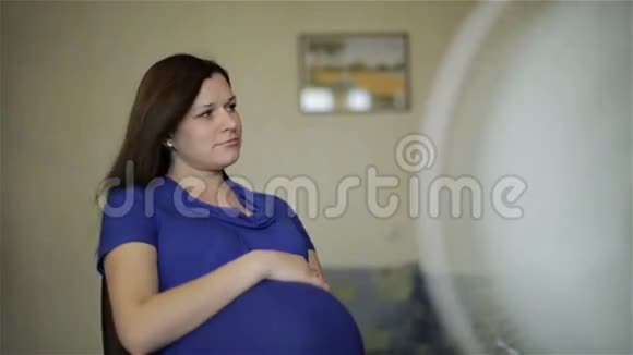 一个穿着蓝色连衣裙的孕妇正在享受风扇的气流视频的预览图