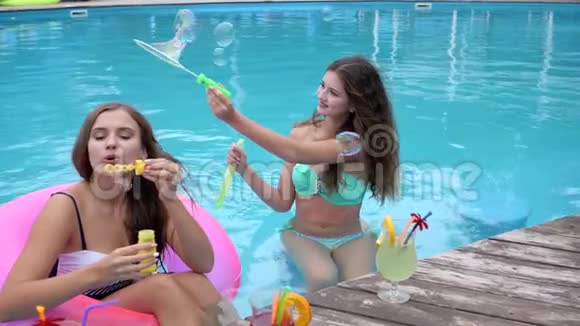 穿着泳衣在游泳池休息的朋友夏天的派对穿着泳衣的女朋友在泳池边吹肥皂泡视频的预览图