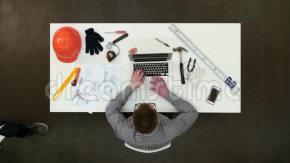 建筑师在笔记本电脑上工作而他的同事带来更多的图纸视频的预览图
