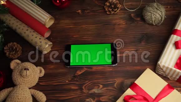 木制背景上景黑色智能手机绿色屏幕躺在桌子上上面假日装饰视频的预览图