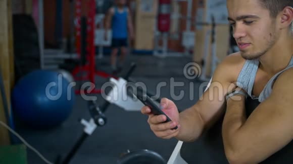 运动员锻炼后坐在健身中心在网上聊天智能手机视频的预览图