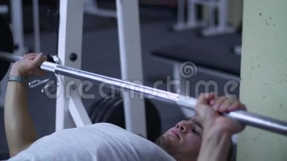 强壮的男性健美运动员在健身房里用沉重的杠铃做长凳按压运动视频的预览图
